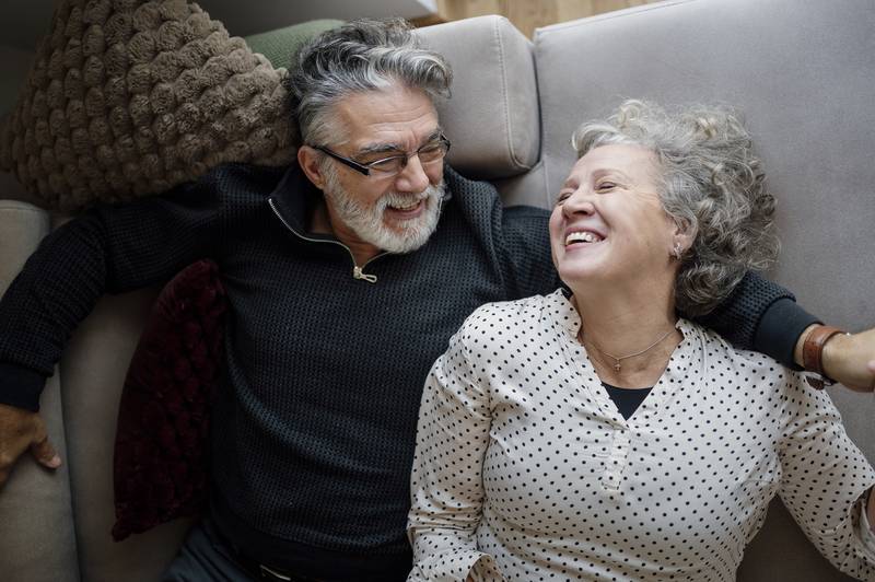 An older couple laughing together while relaxing on a gray sofa at home