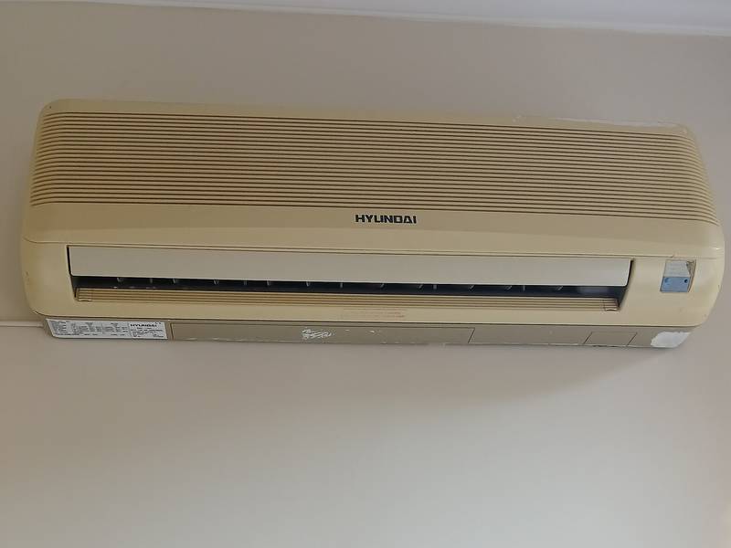 Wall-mounted indoor head of a ductless mini-split air conditioner high on a white wall below the ceiling molding