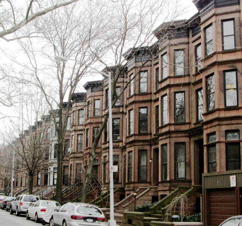 A long row of brownstone row houses with bay windows and high stoops on St. John's Place in Park Slope, Brooklyn, under bare winter trees