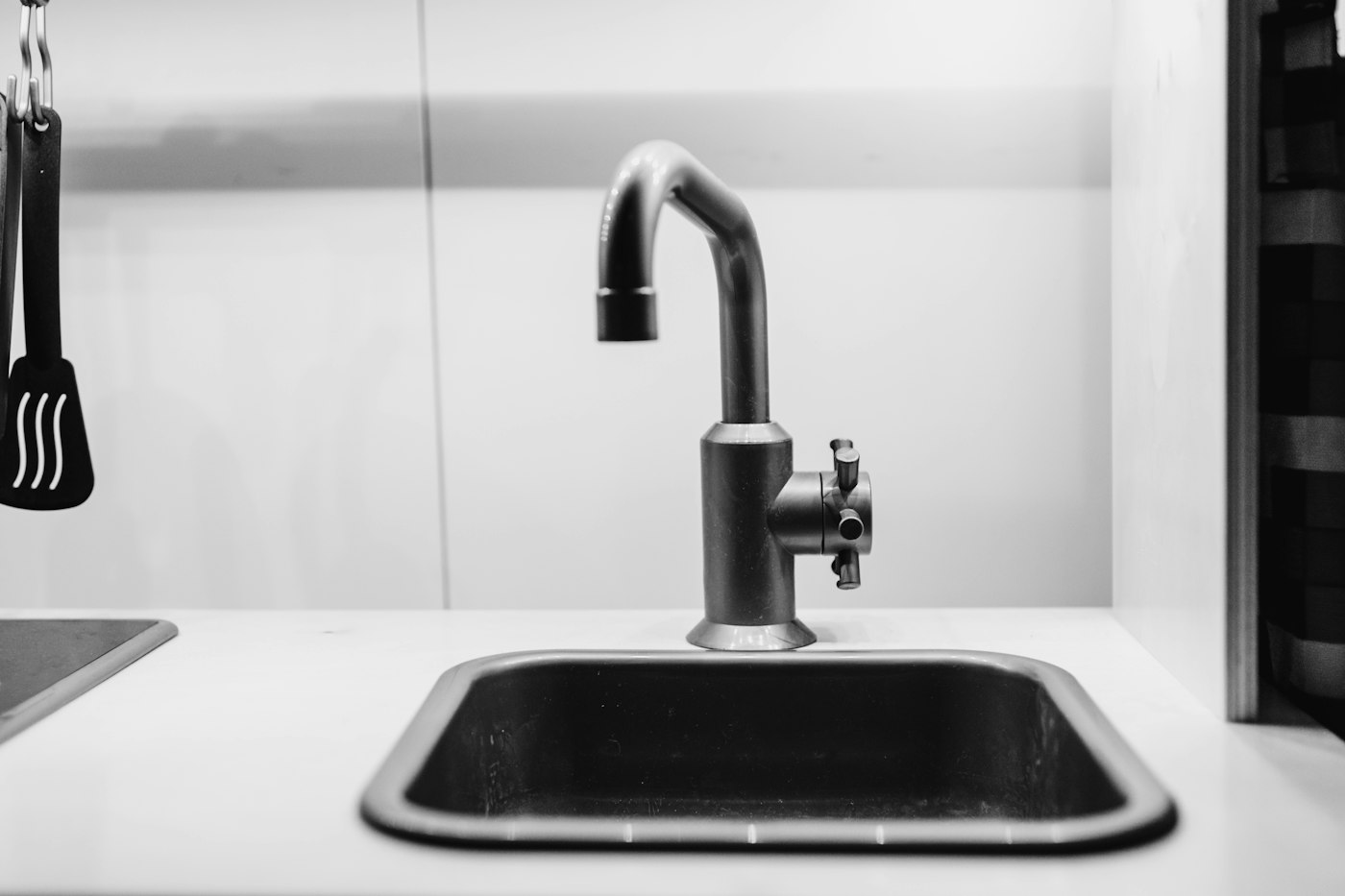 Black and white photo of a stainless steel faucet over a small kitchen sink