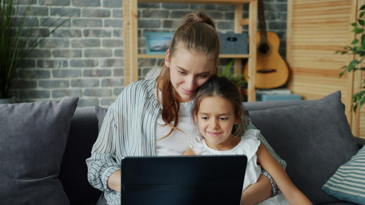 Smiling mother and young daughter sitting together on a sofa looking at a laptop