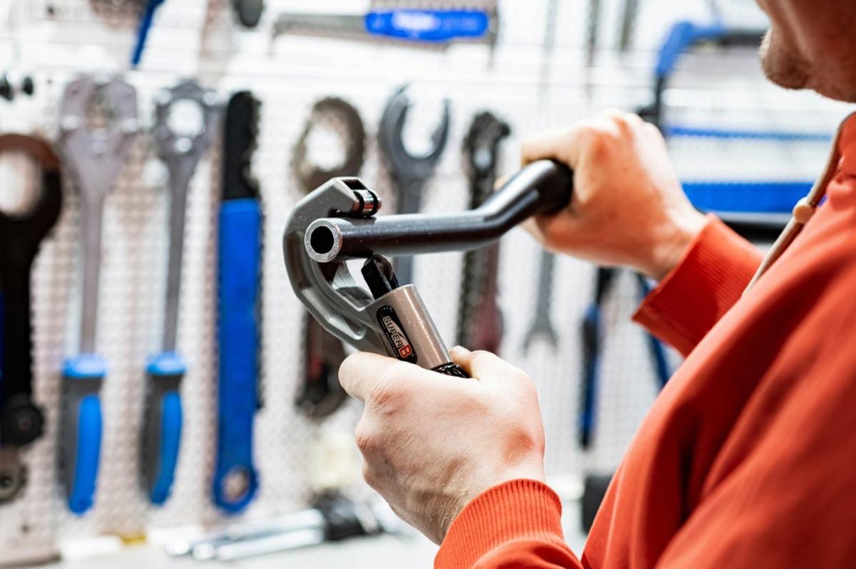 Hands working a pipe cutter in front of a wall of wrenches