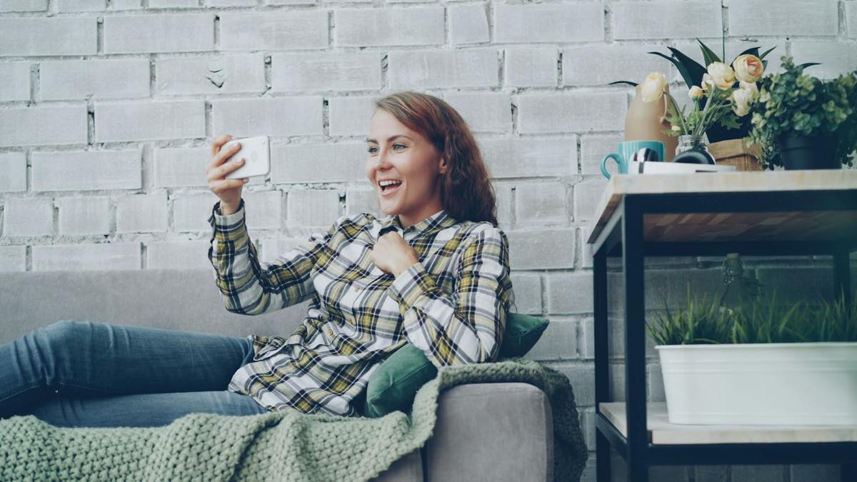 Smiling woman on a sofa at home holding up her phone for a call