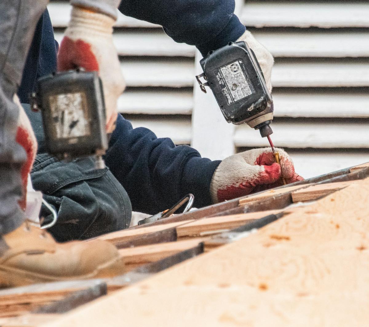 Two roofers in gloves driving screws into new plywood roof decking