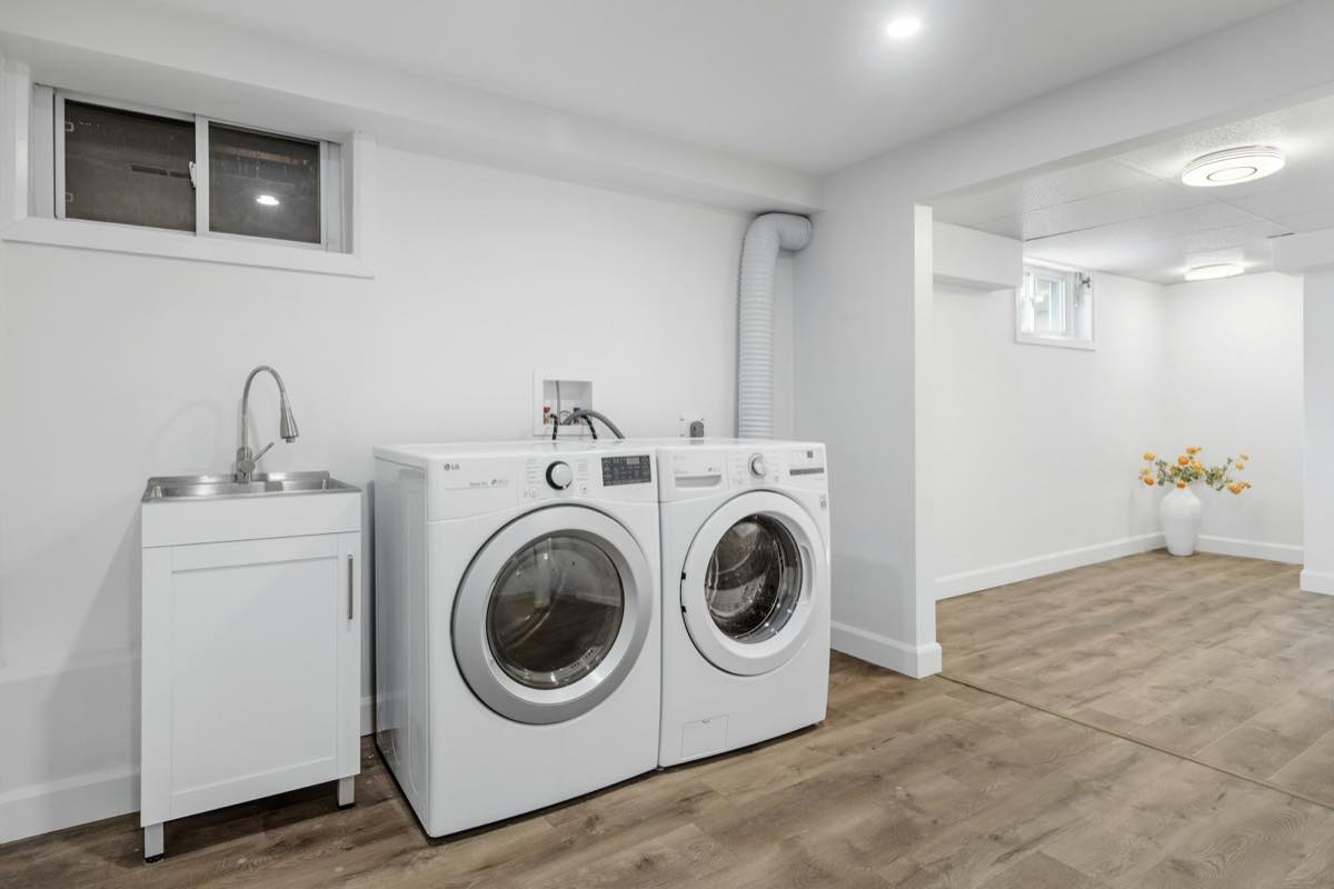 Finished laundry room with front-load washer and dryer, utility sink and dryer vent hose next to a wood-look floor