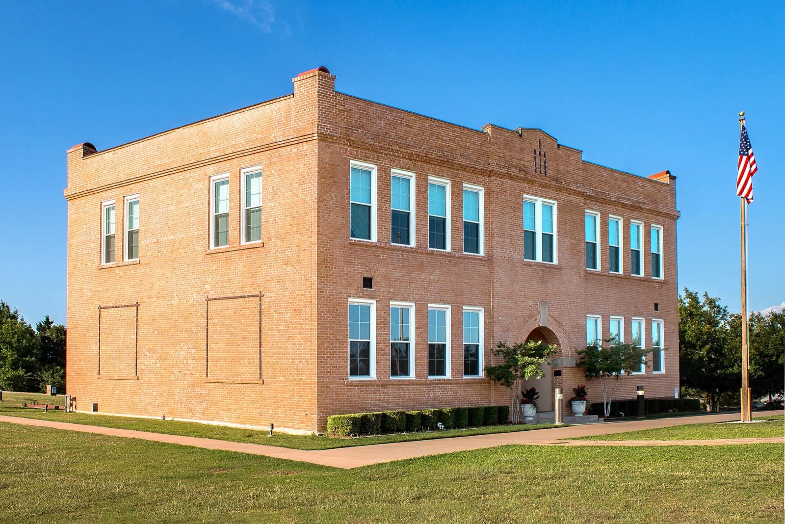 The two-story 1915 brick Old Bedford School on School Lane in Bedford, Texas, under a clear blue sky with the US flag flying