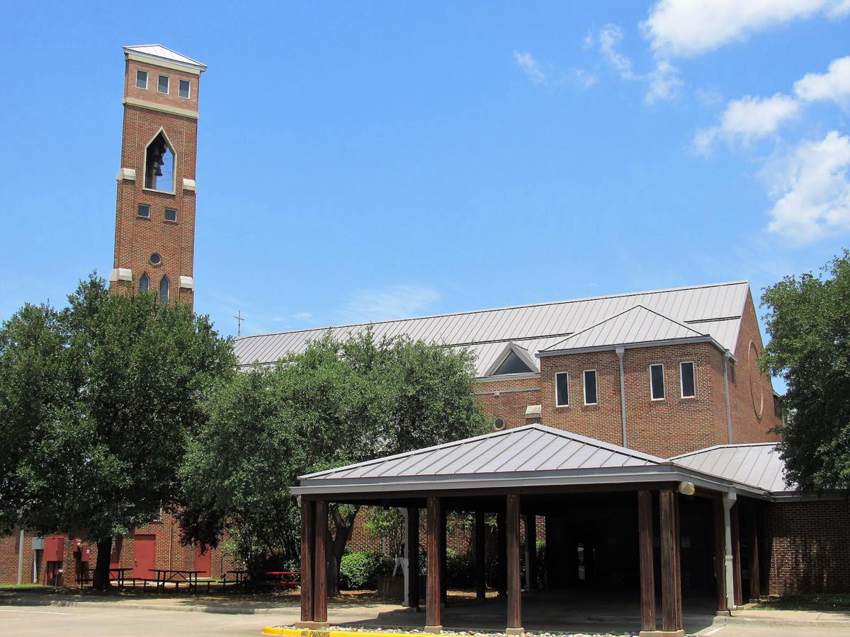St. Vincent's Cathedral in Bedford, TX, with a brick bell tower and covered entry among shade trees