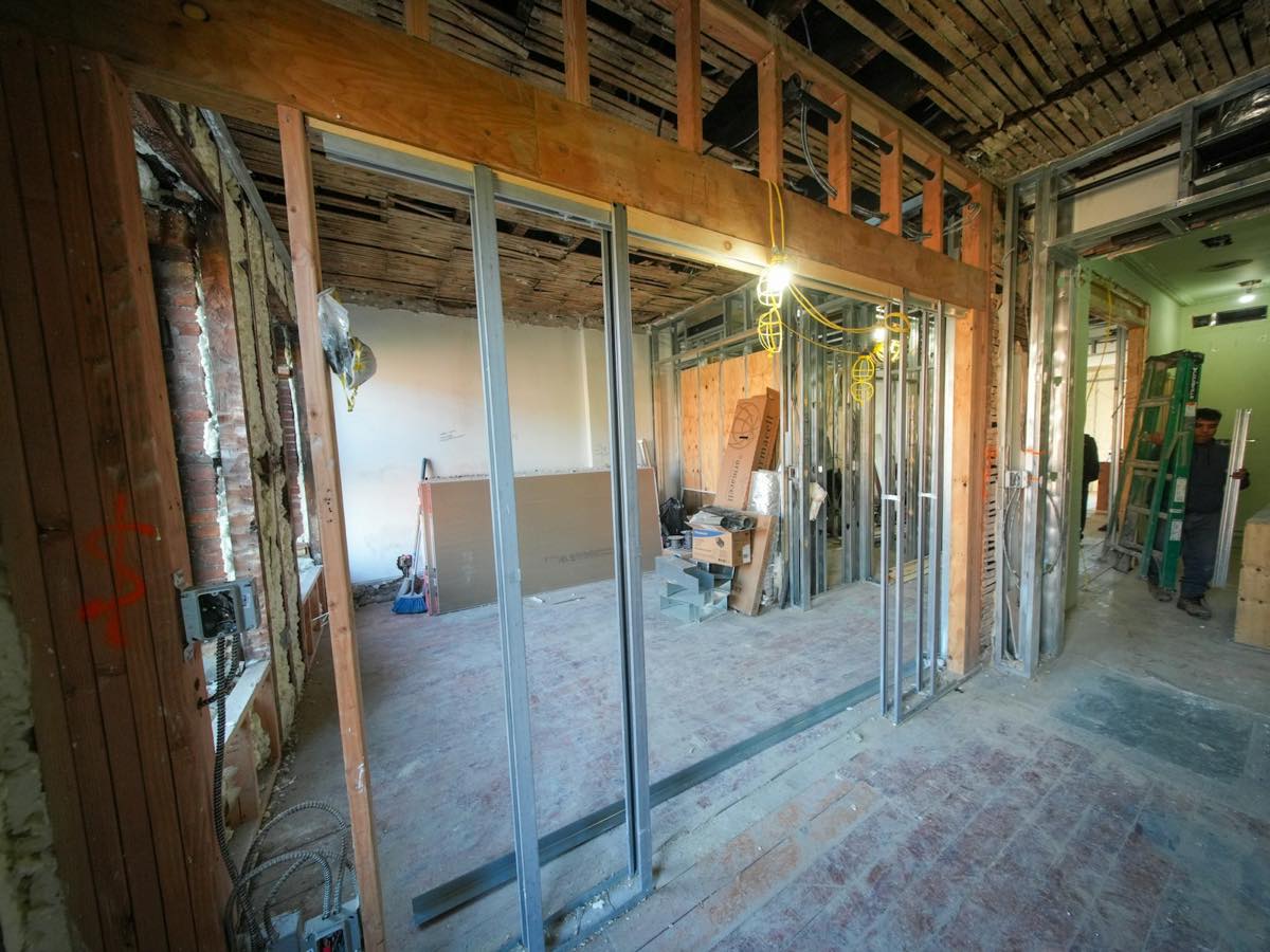 Room stripped to the studs during tear-out, exposed joists and wall framing with tools on the subfloor