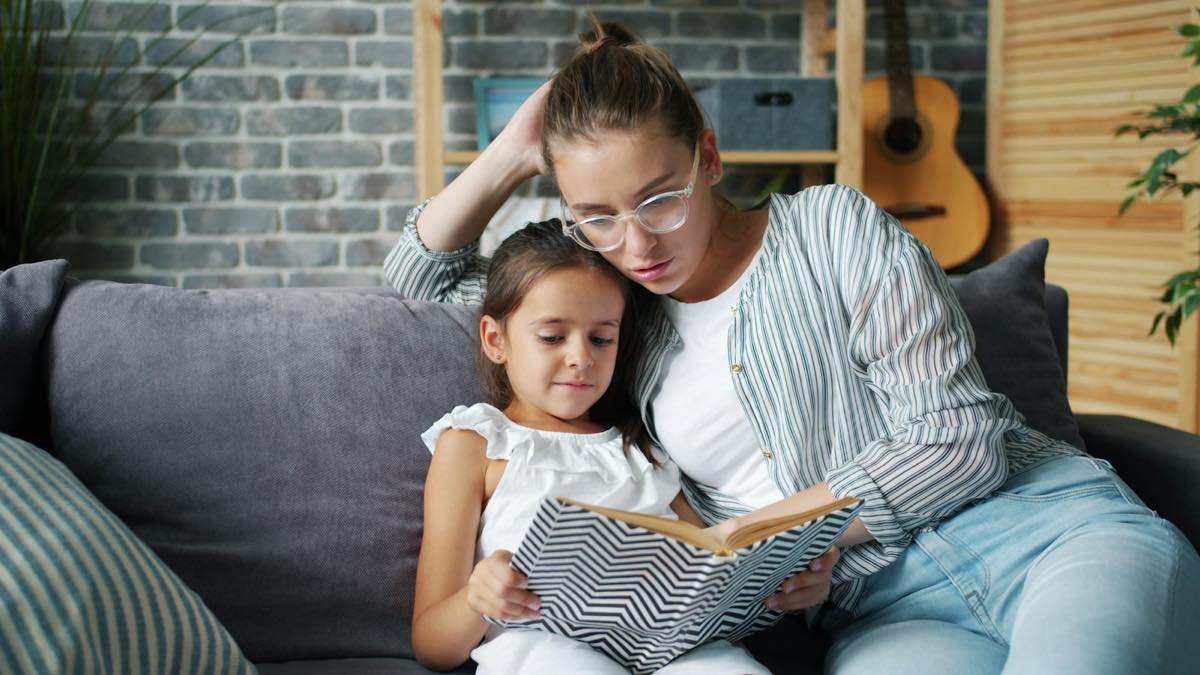 Mother and daughter reading a book together on the living-room couch