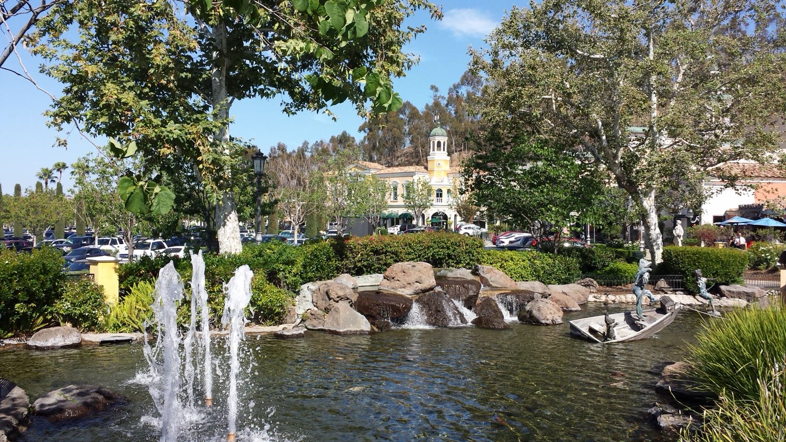 Fountain pond and rock waterfall at The Commons at Calabasas with the yellow bell-tower building behind on a sunny afternoon