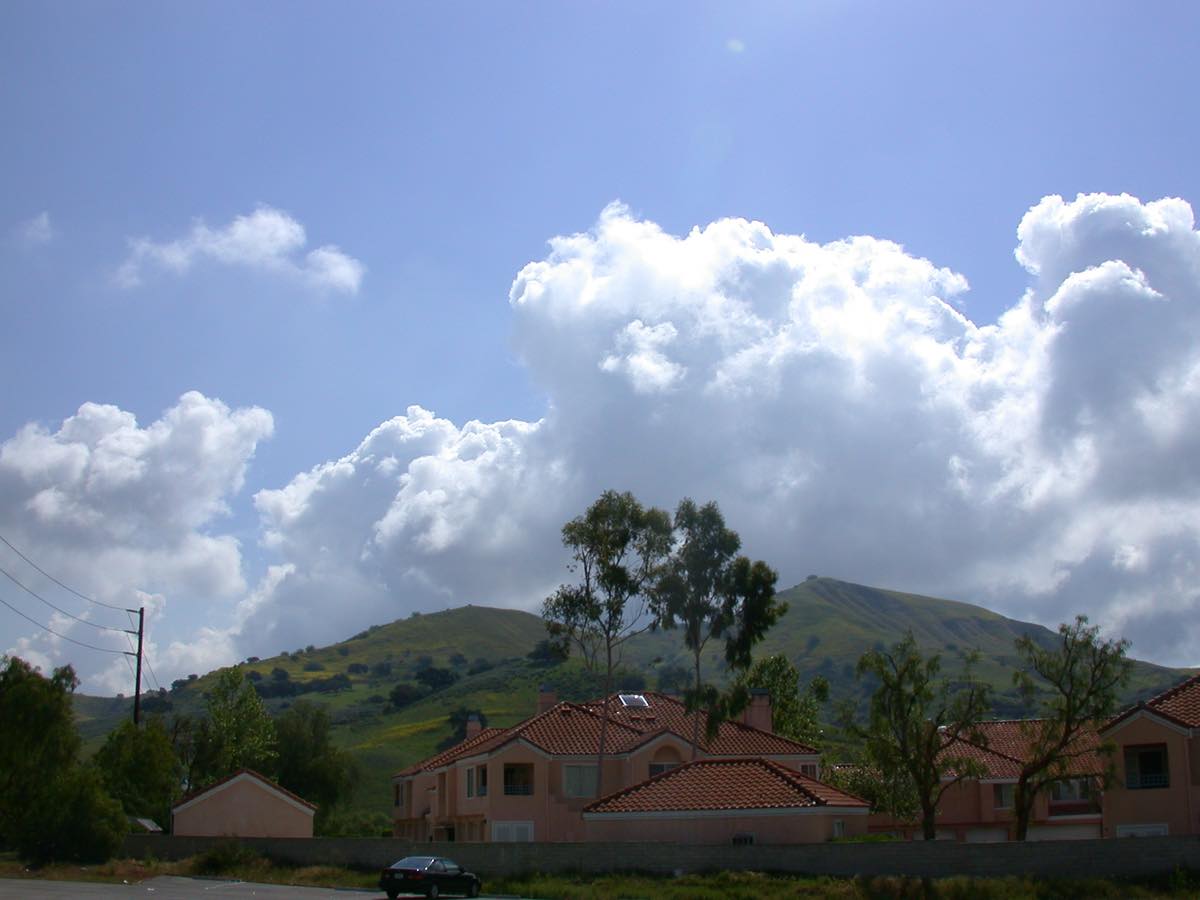 Red-tile-roof Calabasas condos below green Santa Monica Mountains foothills and big cumulus clouds