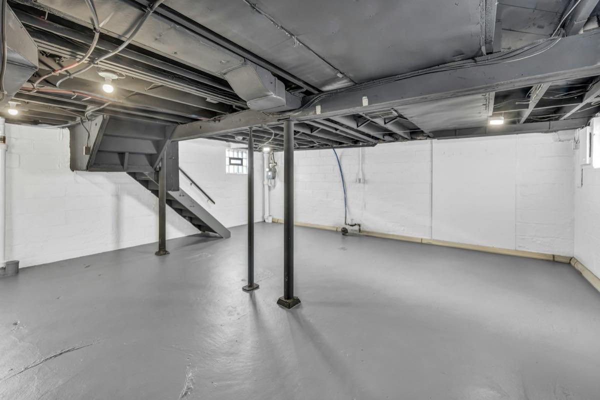 Empty unfinished basement with a painted concrete floor, steel support posts, bare walls and exposed ceiling joists