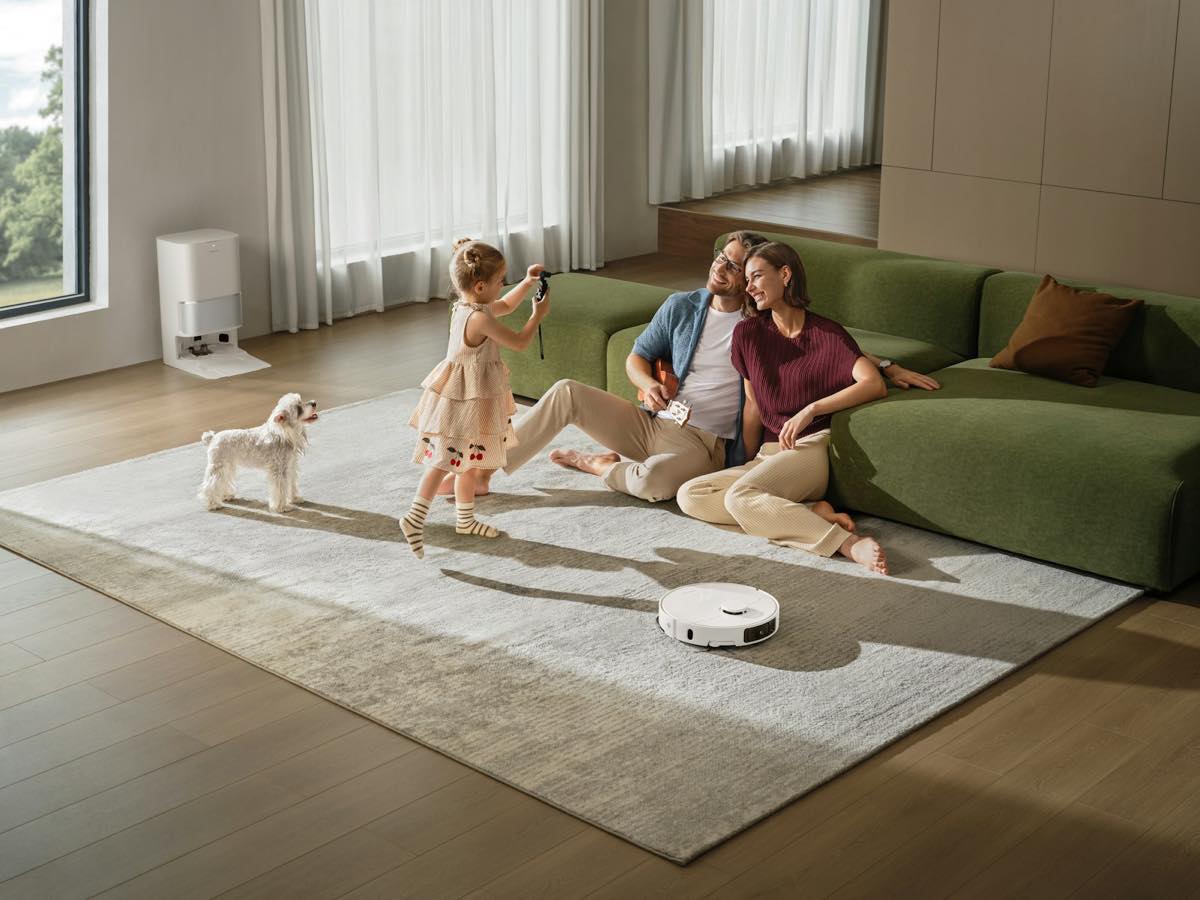 Couple sitting on a rug against a green sofa while their toddler daughter plays with a small white dog in a bright living room