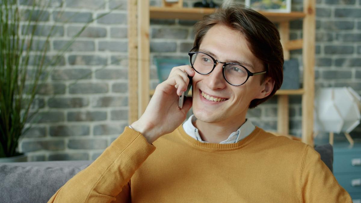 Young man in a mustard sweater on a phone call in his living room