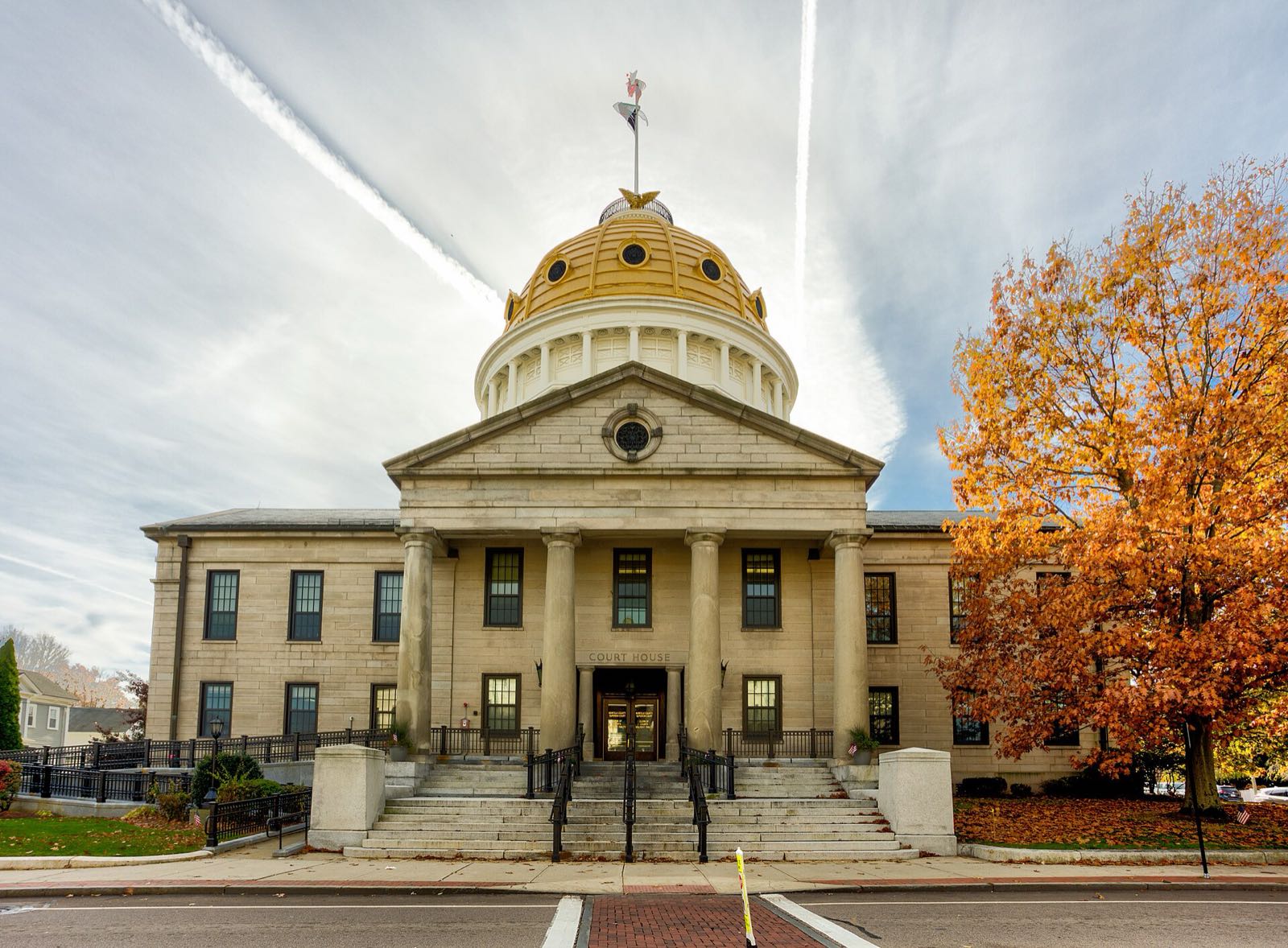 The granite Norfolk County Courthouse with its columns and gilded dome on High Street in Dedham Square, framed by autumn leaves