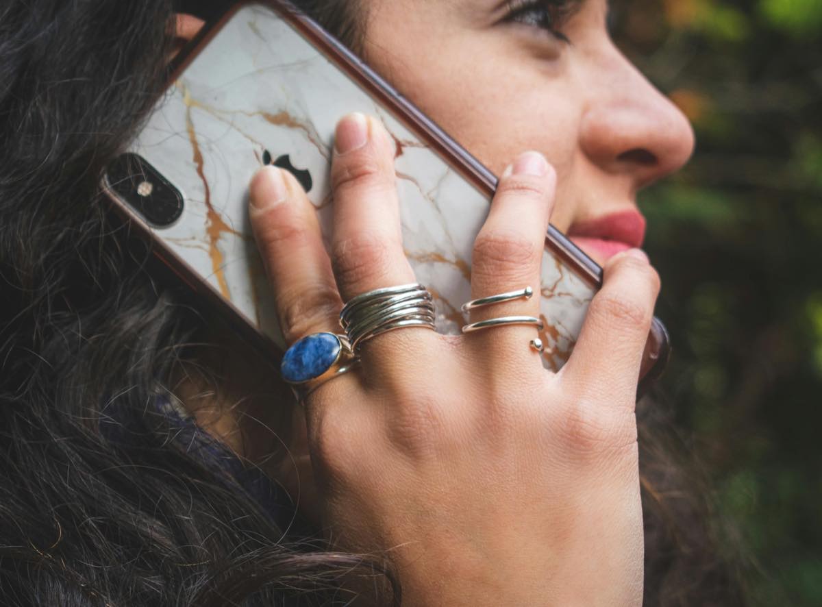 Close-up of a woman holding a smartphone to her ear, her ringed hand pressed against the phone