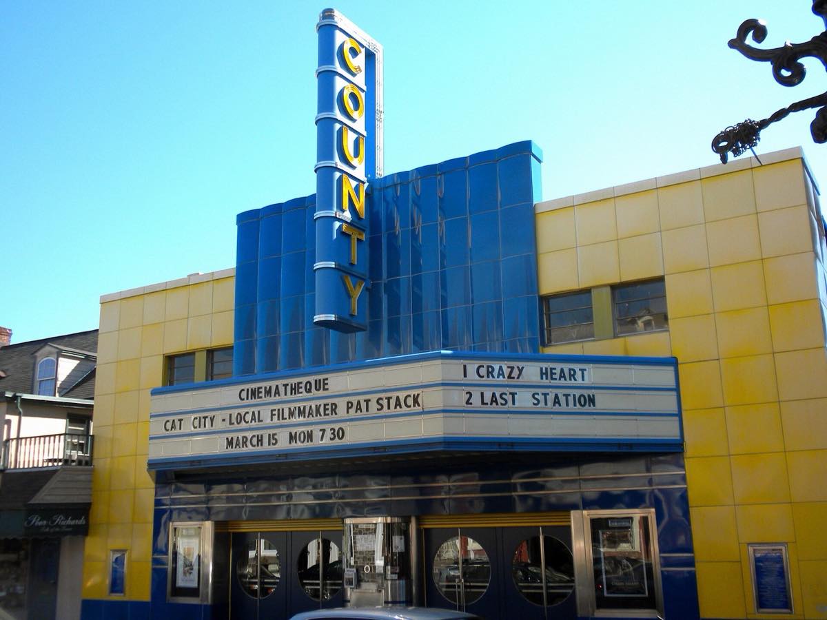 The blue and yellow Art Deco County Theater with its vertical COUNTY sign and marquee on East State Street