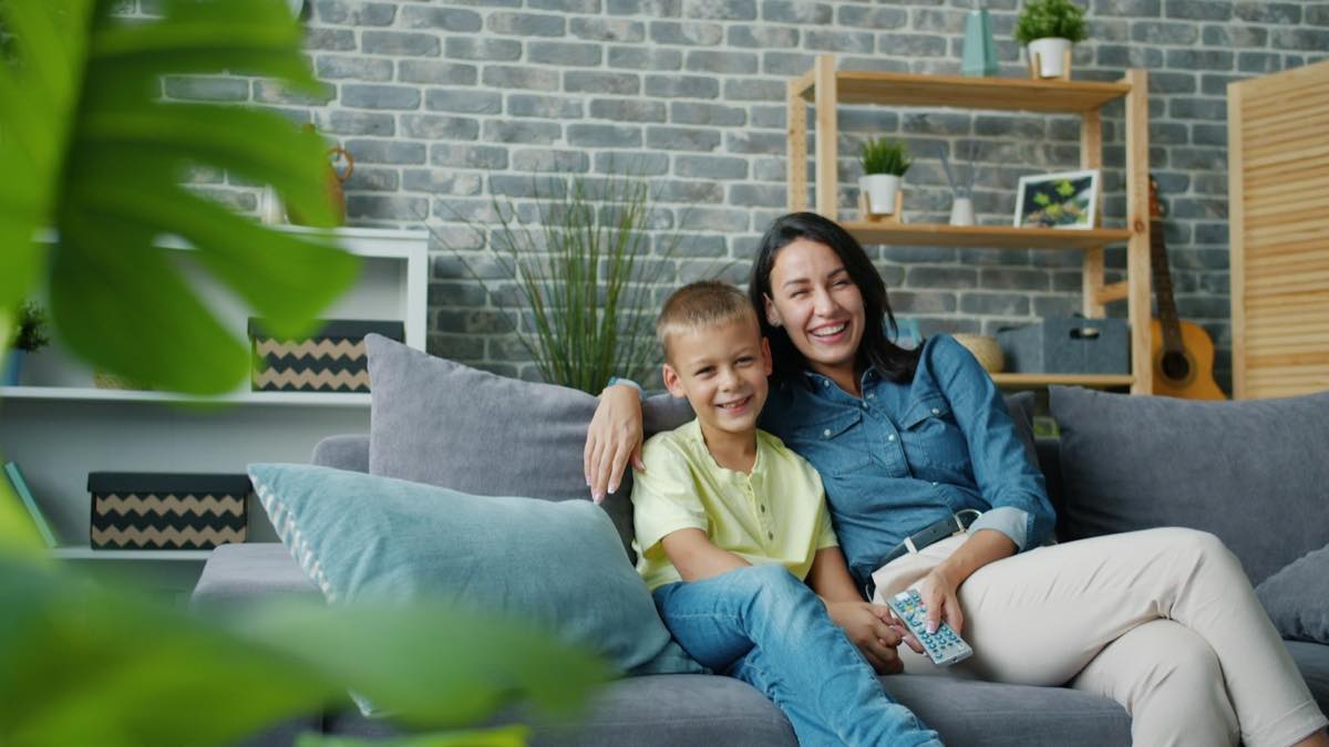 A smiling mother and her young son sitting together on a gray couch at home