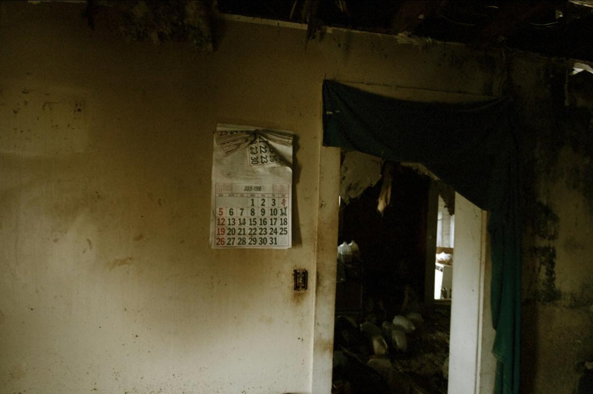 Dim flood-damaged room with stained walls, a warped wall calendar and a collapsed ceiling over the doorway