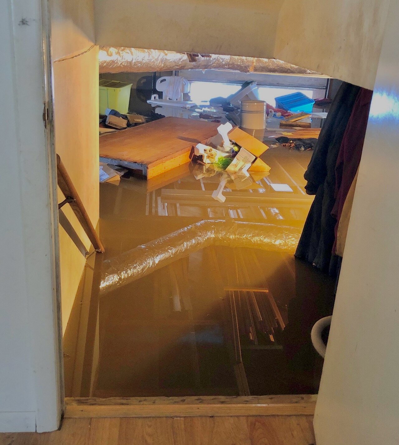 View down the basement stairs into a cellar under murky standing water, with boxes and a duct floating