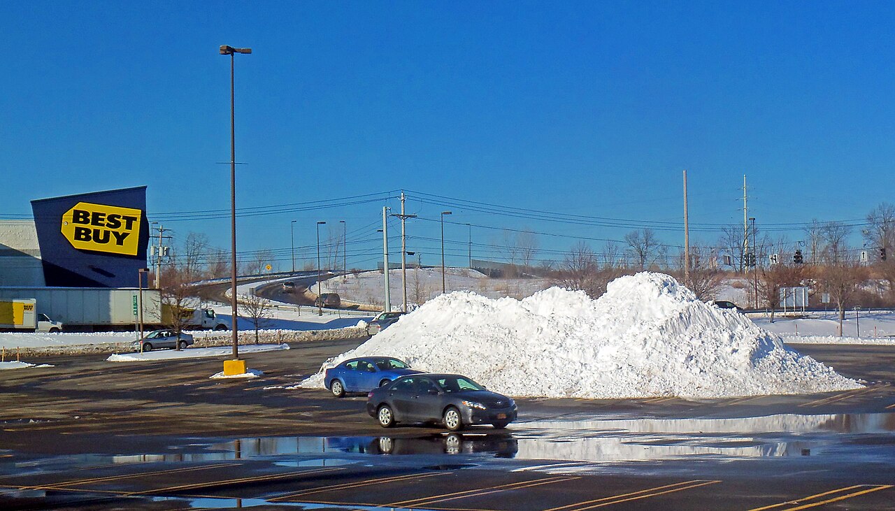 Big plowed snow pile in a shopping-center parking lot with meltwater pooling across the asphalt (Middletown, NY, February 2013)