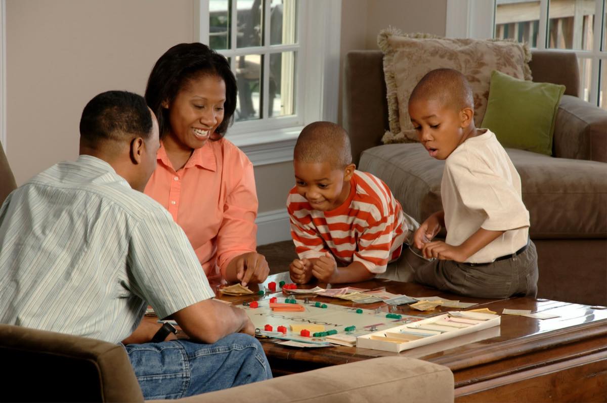Parents and two young sons playing a board game on the coffee table in a bright living room