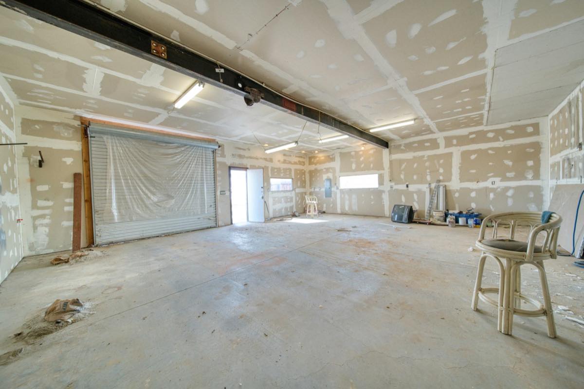 Large room stripped to freshly taped drywall and a bare concrete floor during rebuild