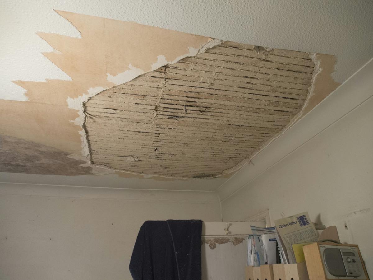 Bedroom ceiling with a large section of drywall torn away, exposing the old lath above