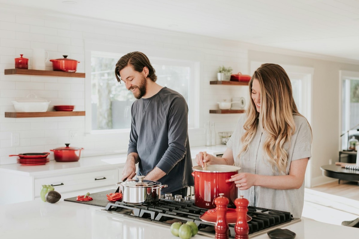 Smiling couple cooking together at the stove in a bright white kitchen