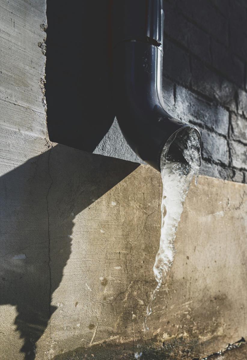 Ice frozen solid at the mouth of a downspout against a brick wall