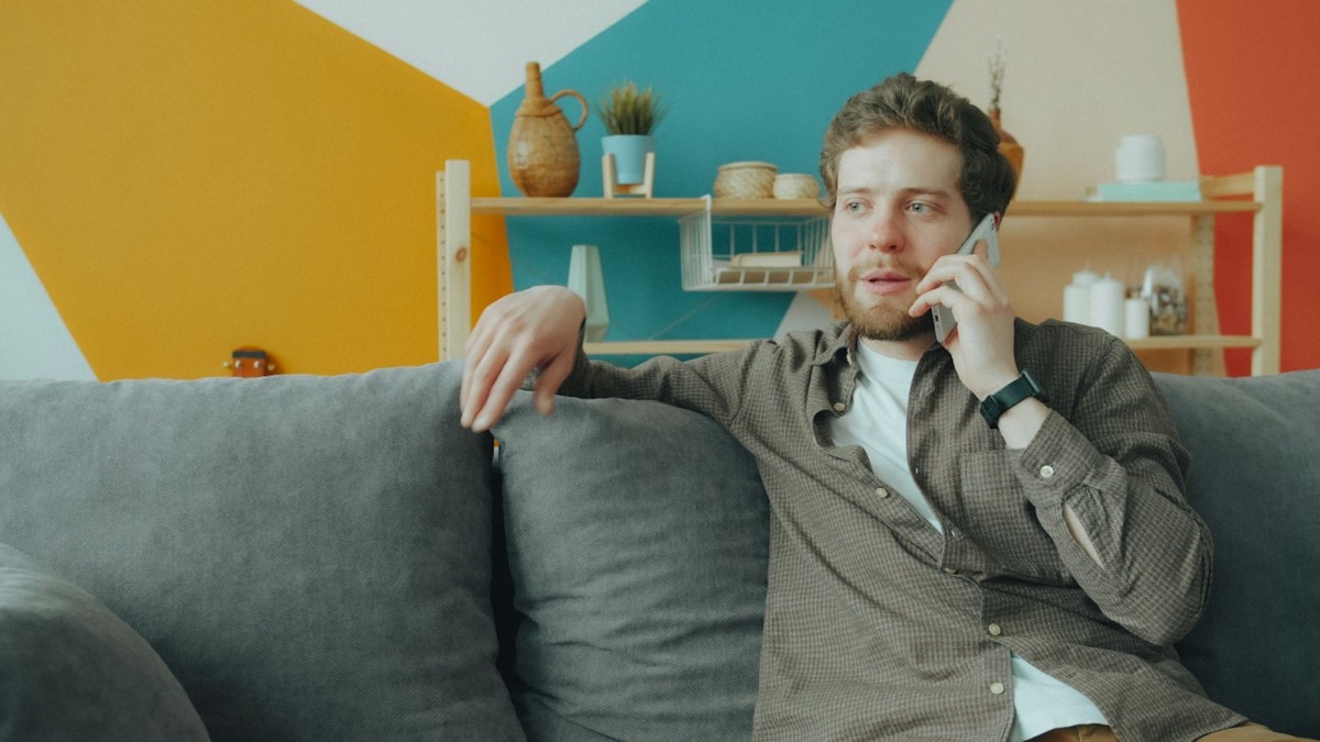 Bearded man sitting on a gray sofa at home, talking on his phone