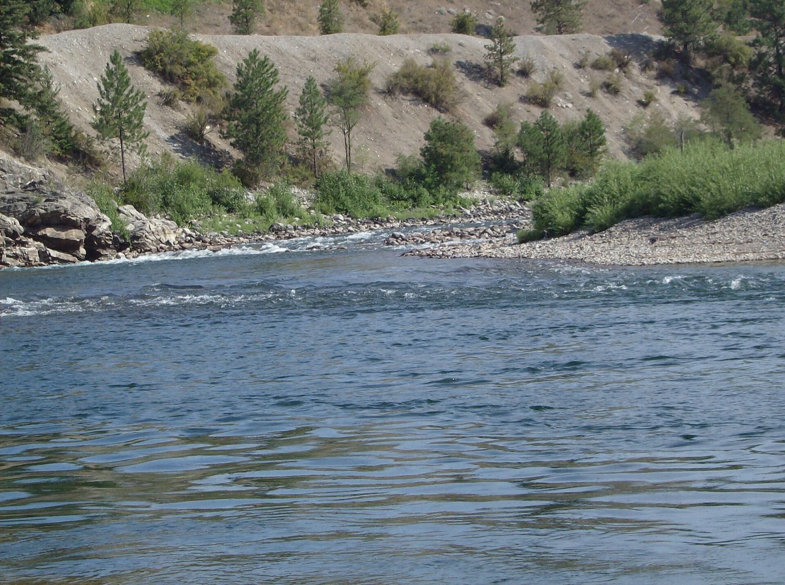 The Spokane River running past the rocky bank at Corbin Park in Post Falls on a bright summer day