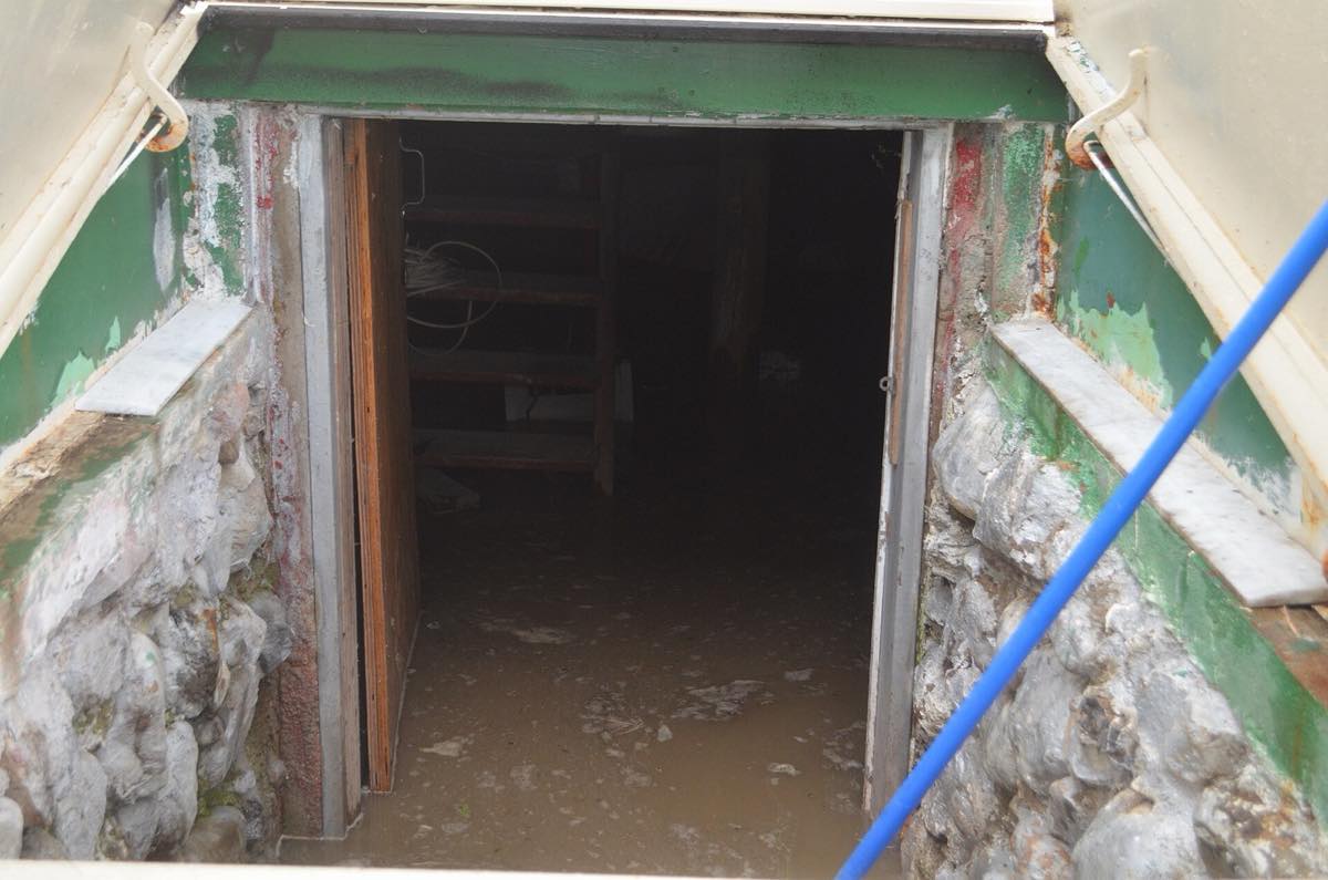 Open cellar door between fieldstone foundation walls, with muddy floodwater covering the basement floor inside