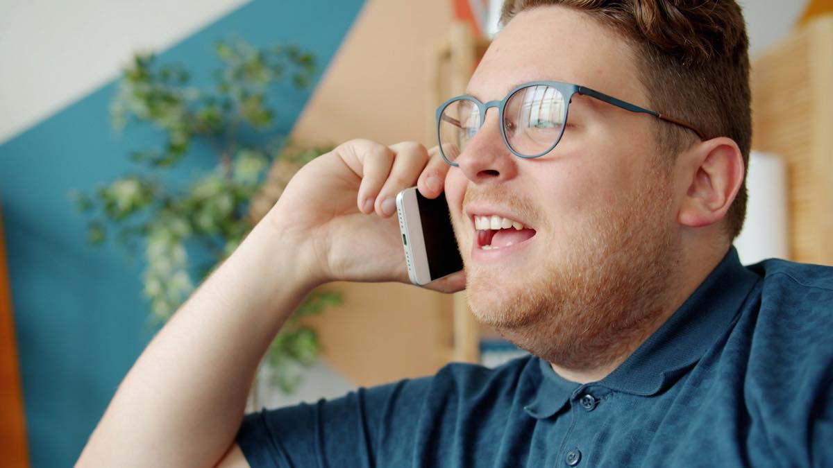 Smiling man in glasses and a navy polo talking on a smartphone at home