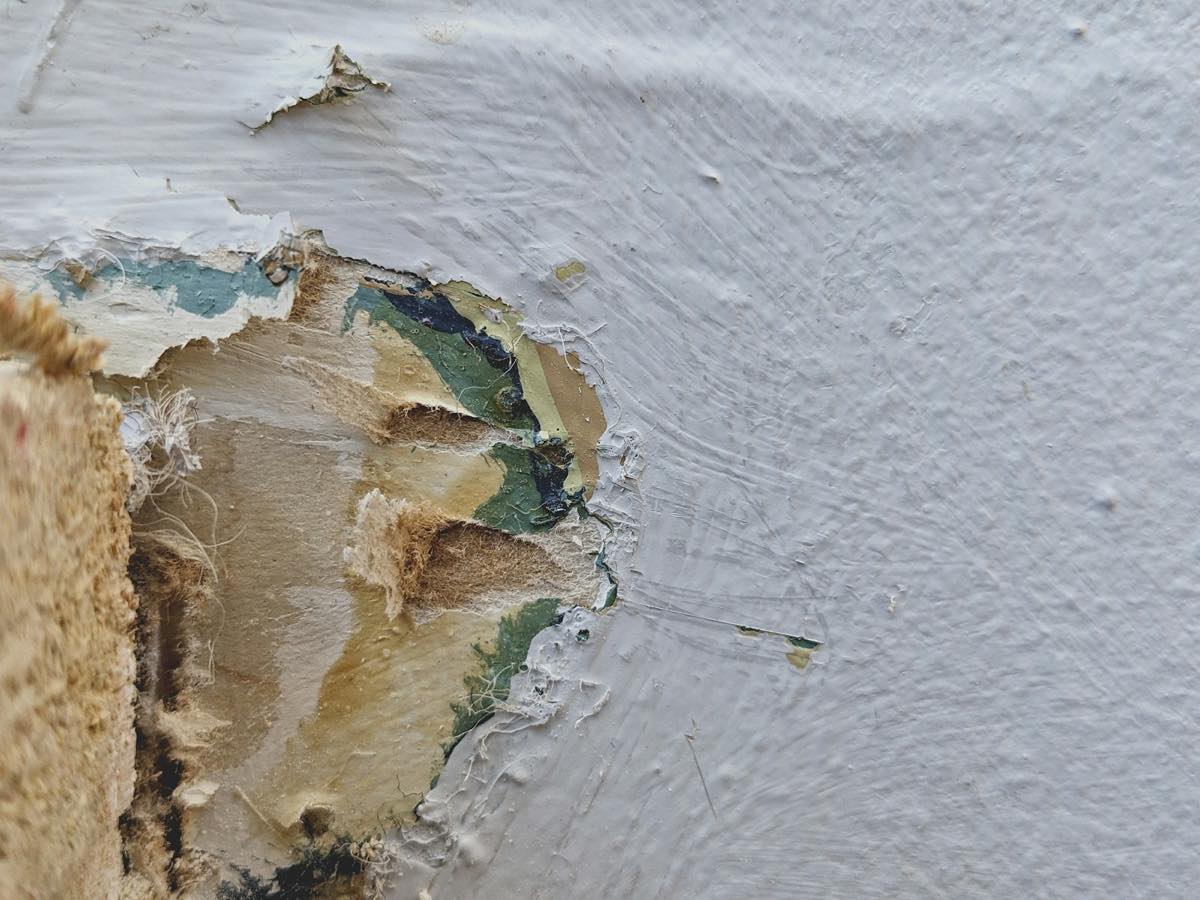 Close-up of a wall where paint and drywall paper have bubbled and peeled away from moisture damage