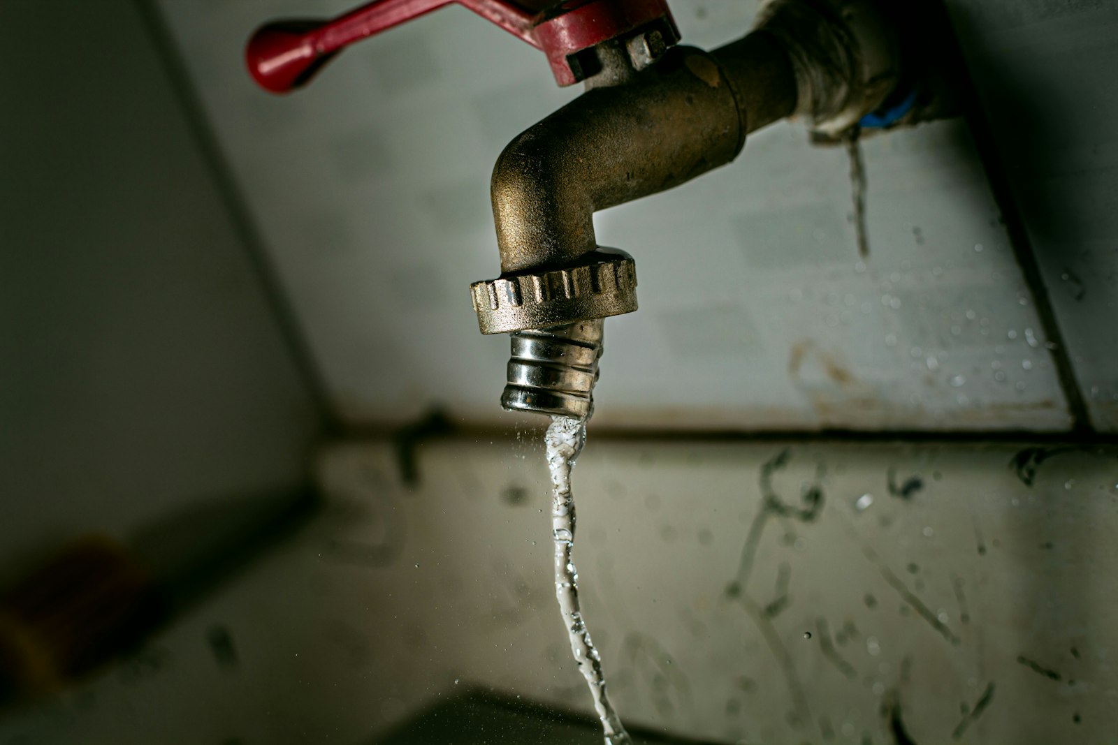 Brass spigot with a red handle running water down a stained wall