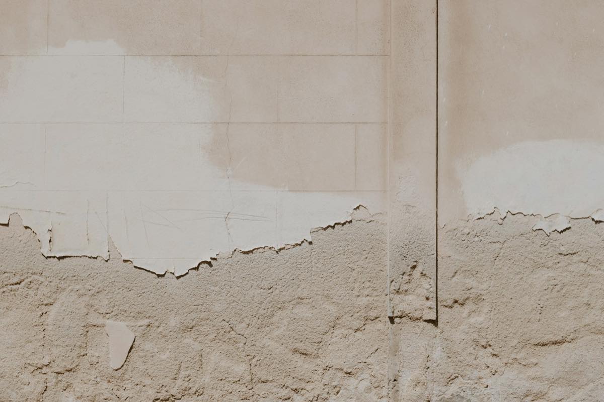 Beige wall with paint and plaster peeling away along a tide line, the kind of damage moisture leaves