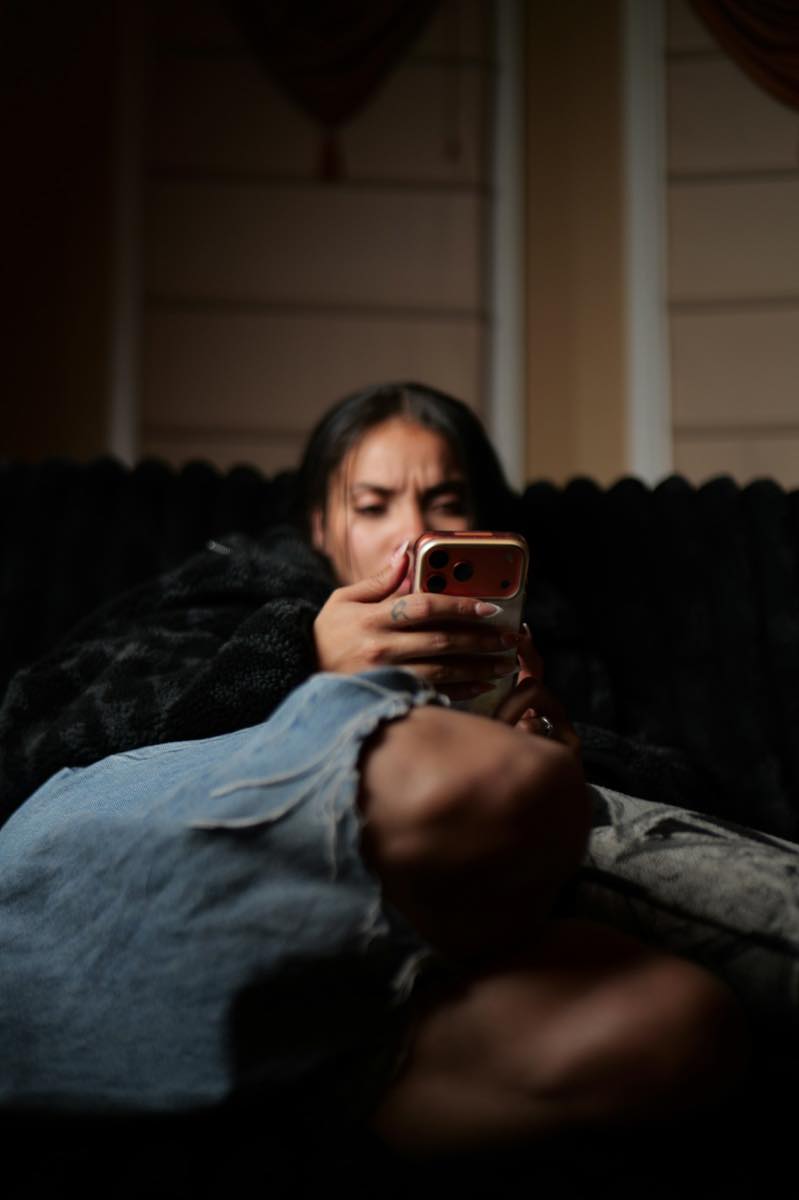 A woman in a fleece jacket curled up on a couch, frowning at her smartphone
